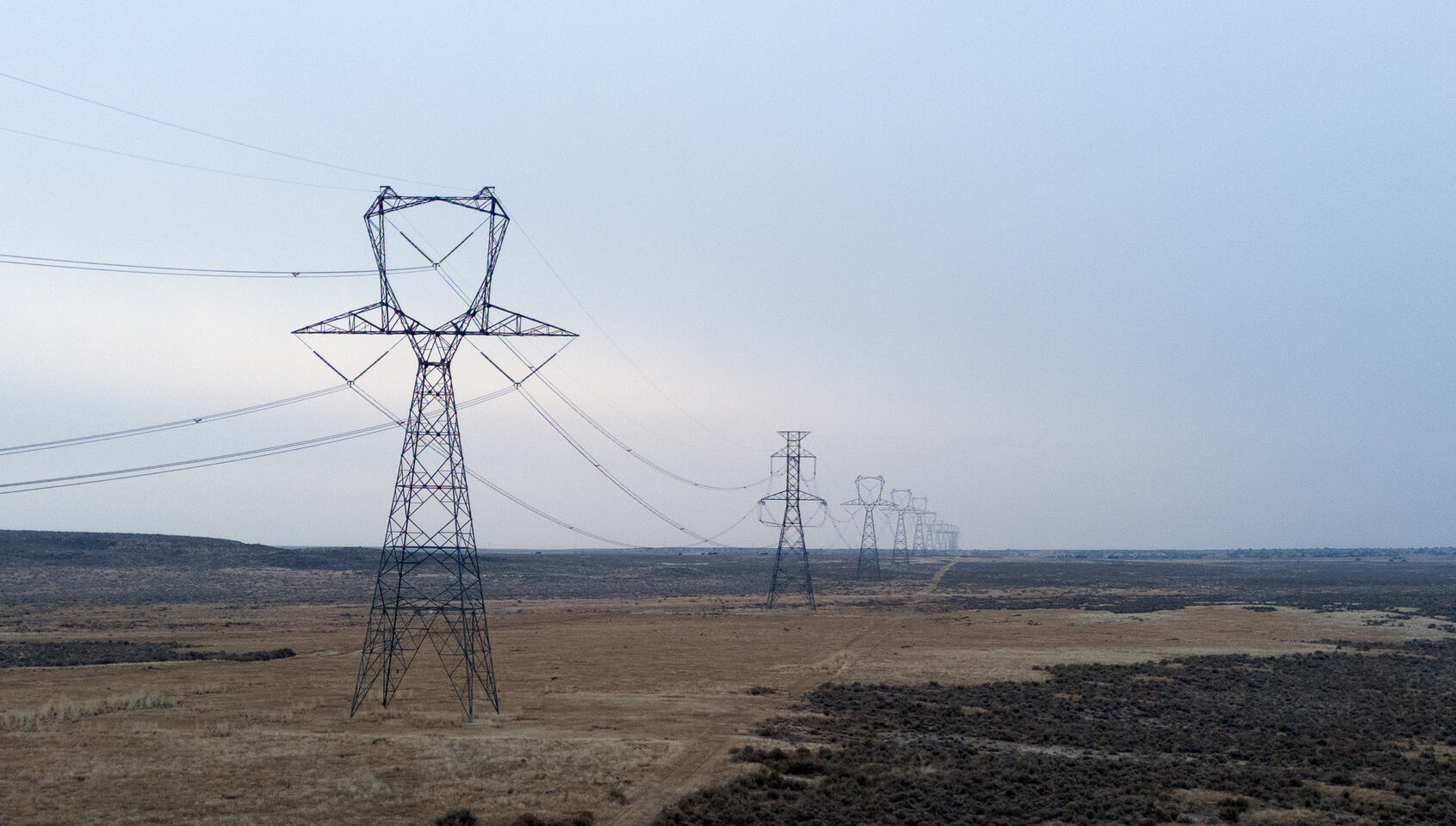 Steel transmission towers stretching into the distance over dry, open landscape.