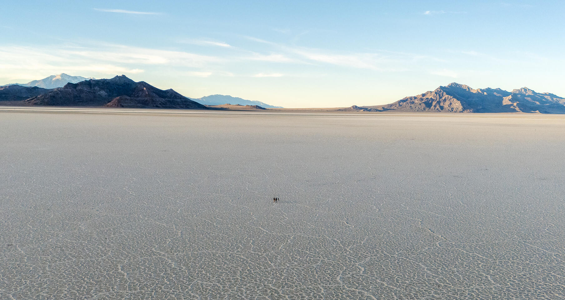 Expansive salt flat with textured surface leading to mountains under a blue sky.