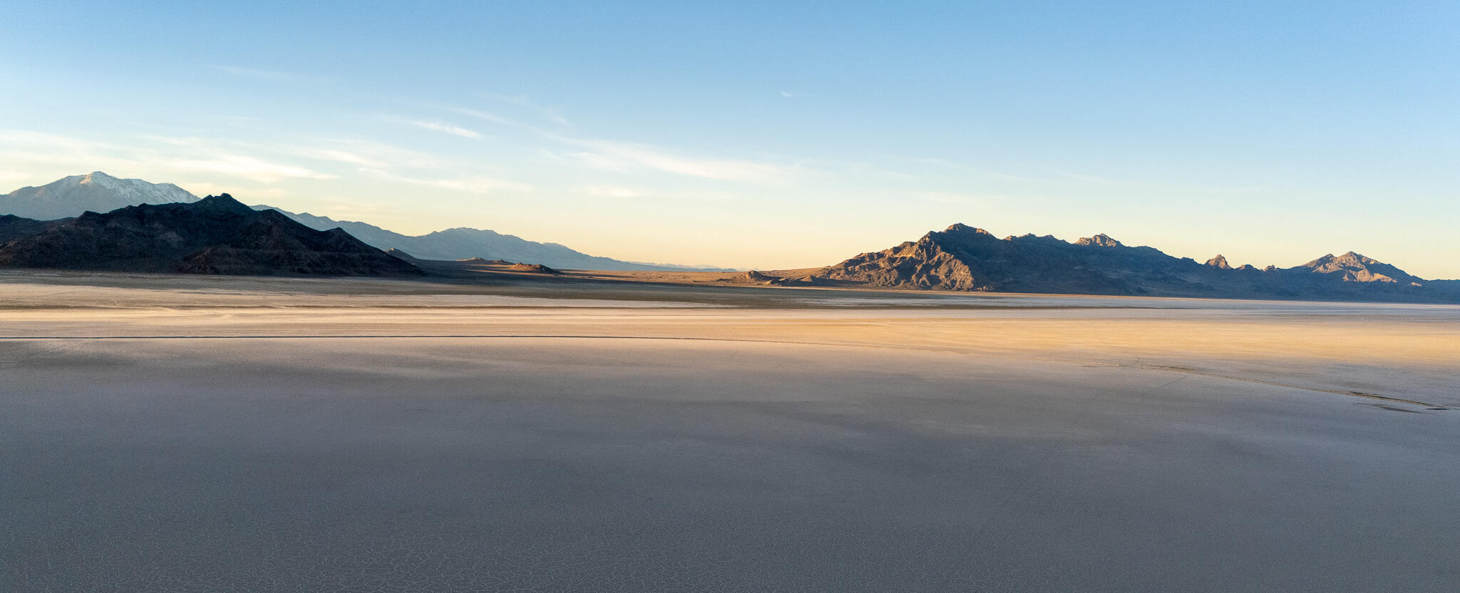 Wide view of salt flats under early evening light with distant mountain range in silhouette.